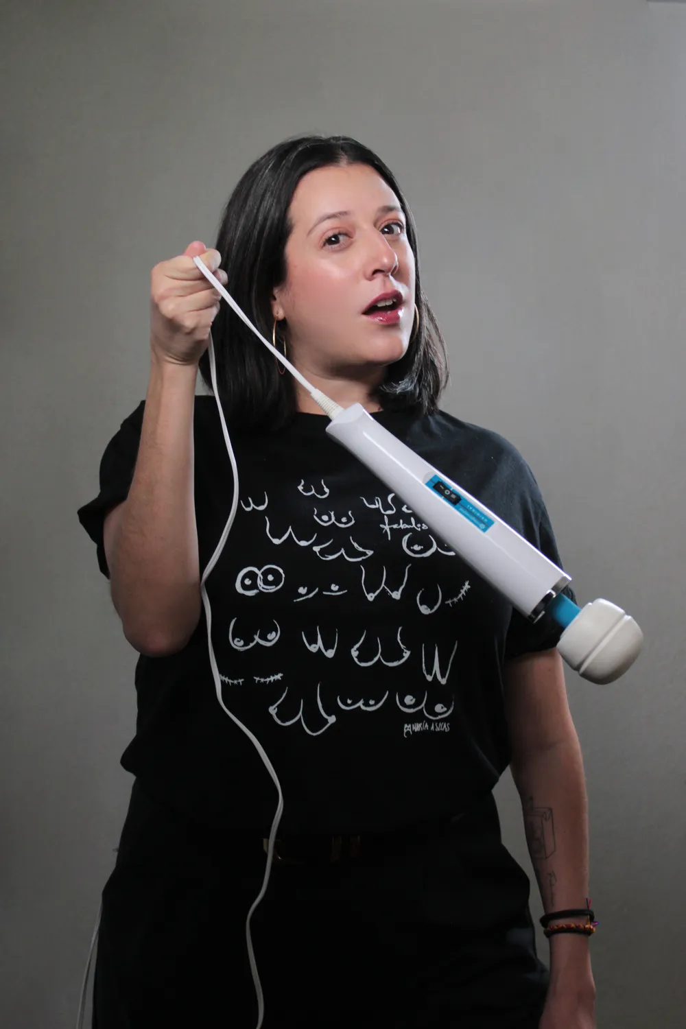 María A Secas con una playera ilustrada sosteniendo un masajeador como si fuera un micrófono